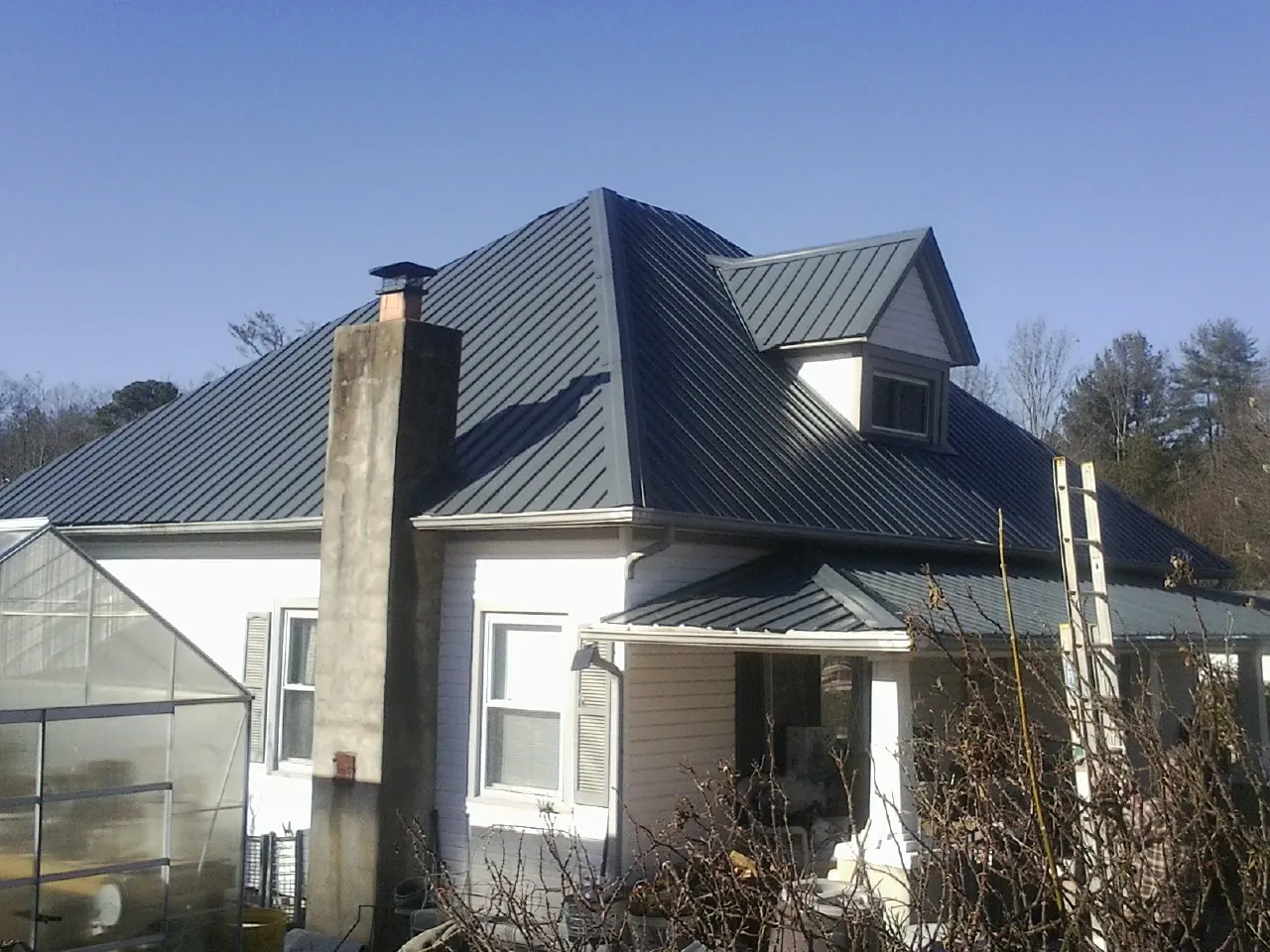 Dark blue standing seam metal roof on a white farmhouse with dormer — Slate & Tile Roof Repair by Roofing Brothers in Colmar
