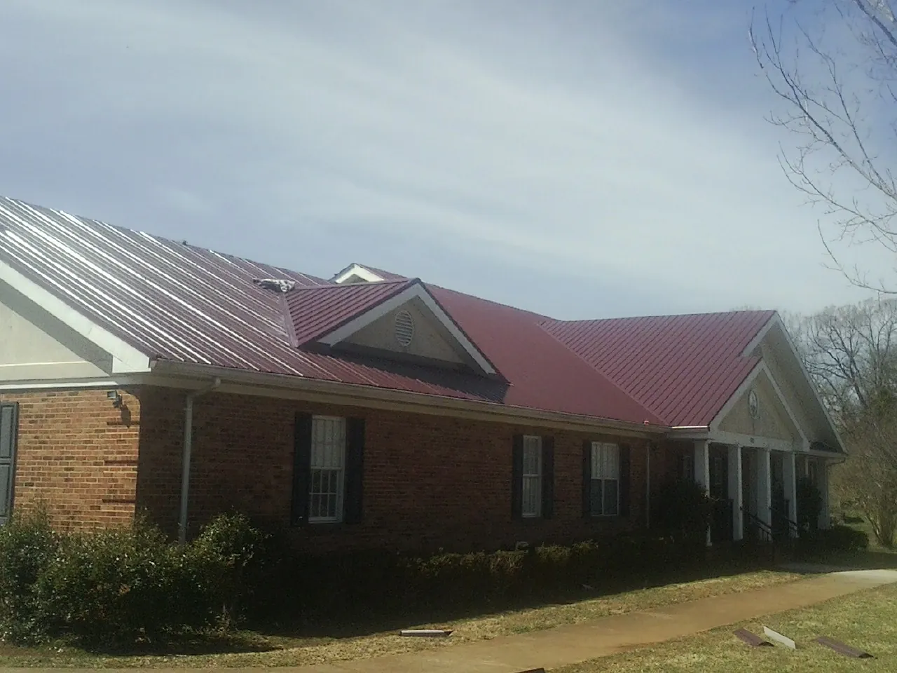 Red metal roof with gabled entries on a long brick building, from a Hail Damage Roof Repair job in Colmar