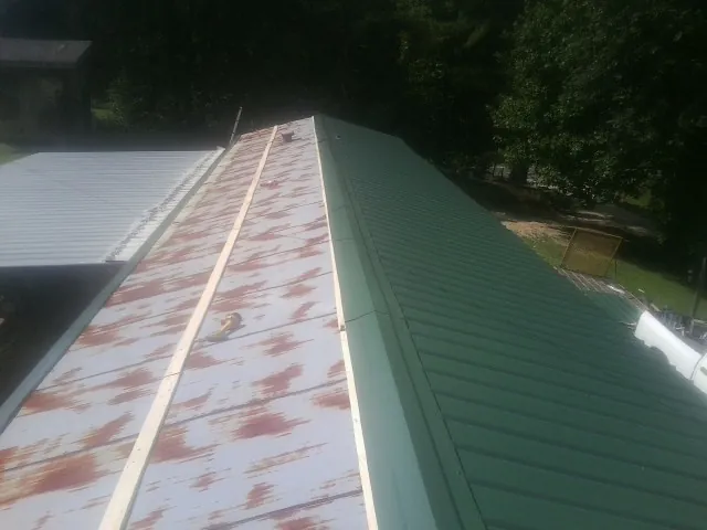 Old rusted panels beside newly installed green metal roofing — Wind Damage Roof Repair by Roofing Brothers in Colmar