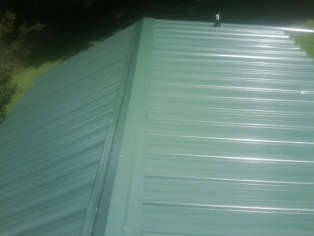New green metal panels meeting at the ridge of a roof — Flat Roof Repair work by our crew in Colmar