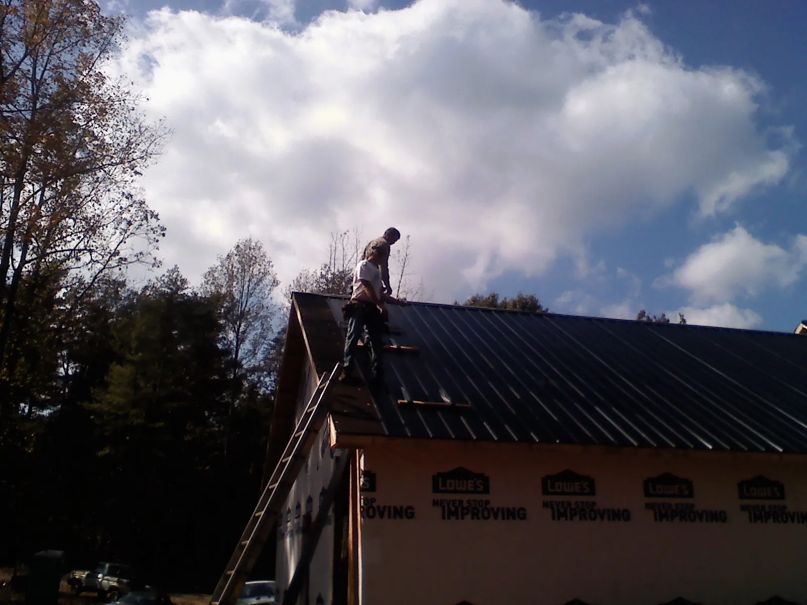 Roofer fastening dark metal panels high against a cloudy sky, from a Roof Inspection job in Colmar
