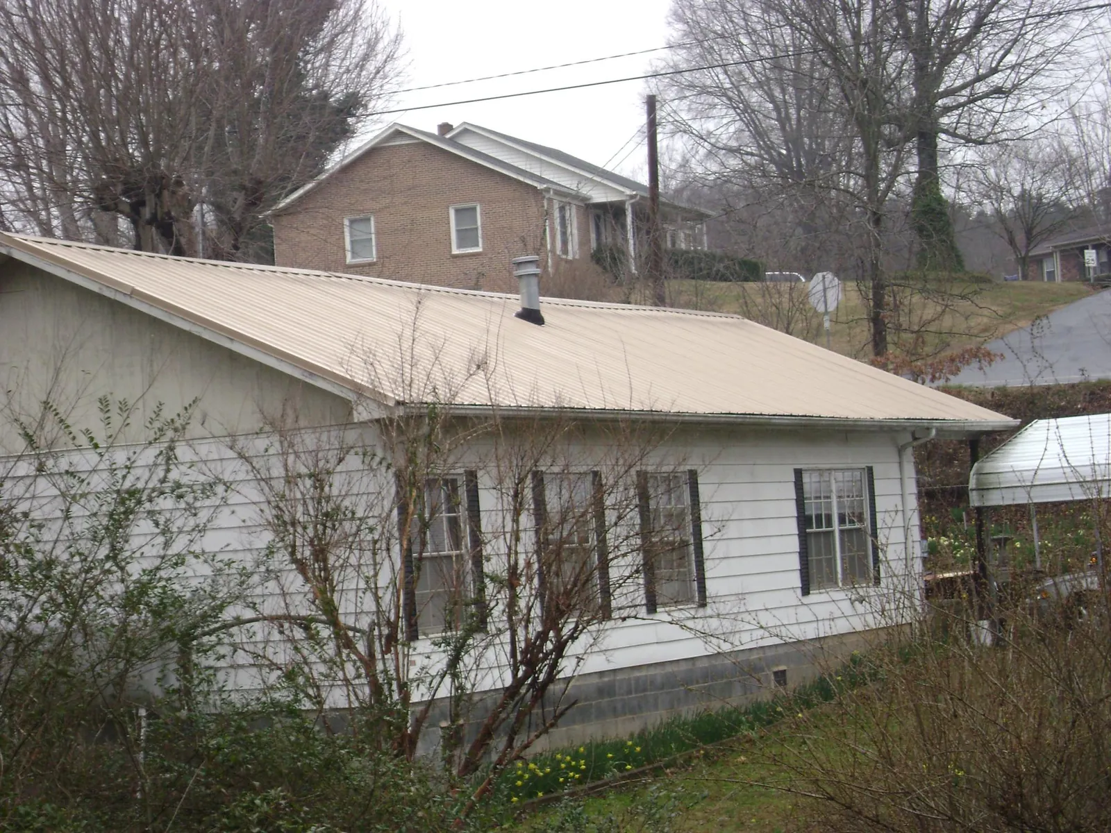Tan metal roof on a white sided house set into a hillside — Commercial Roofing by Roofing Brothers in Colmar