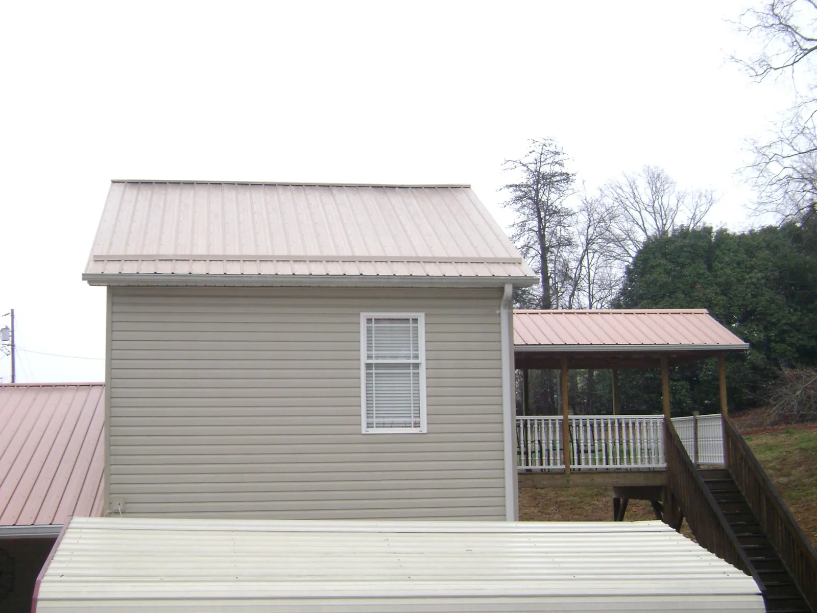 Tan metal roofs on a two story addition and attached porch, from a Roof Replacement job in Colmar